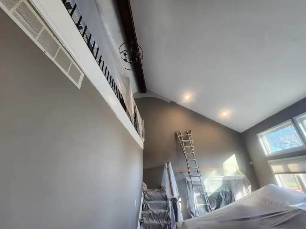 Residential interior painting in progress with vaulted ceiling, covered furniture, and ladder by PaintWerks