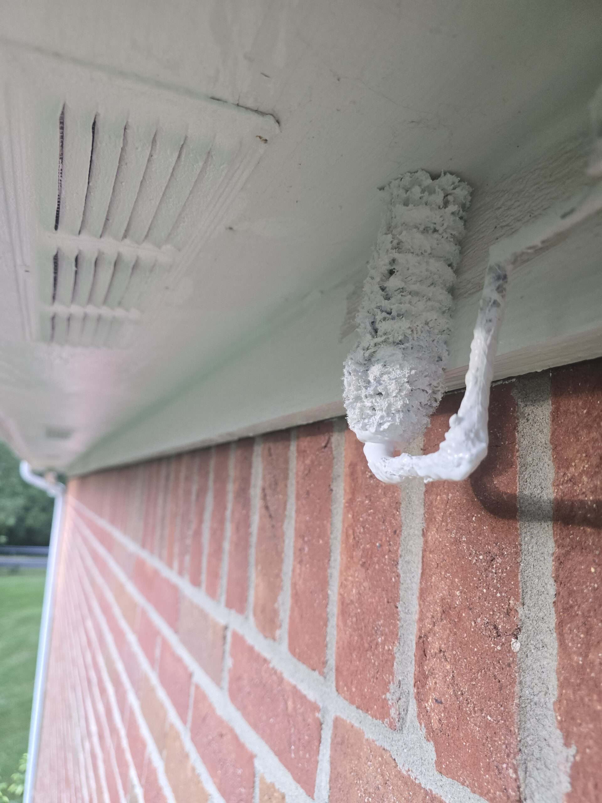 Close-up of house painting process showing paint roller applying white paint on the soffit beneath the roof gutter.