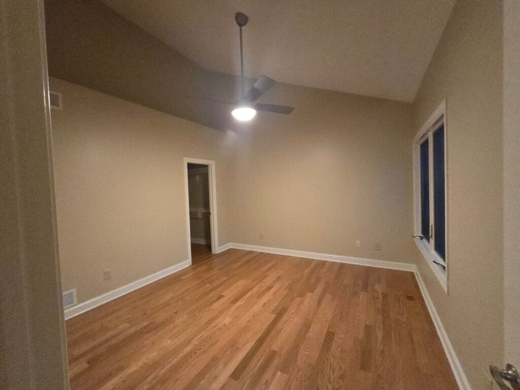 Bright, clean room with freshly painted beige walls, ceiling fan, and hardwood flooring.