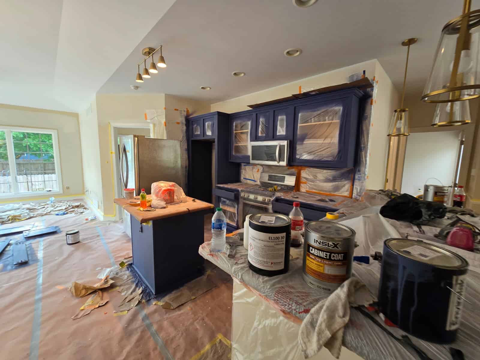 Brightly lit kitchen with blue cabinets and ongoing interior paintwork, showcasing professional house painting services.