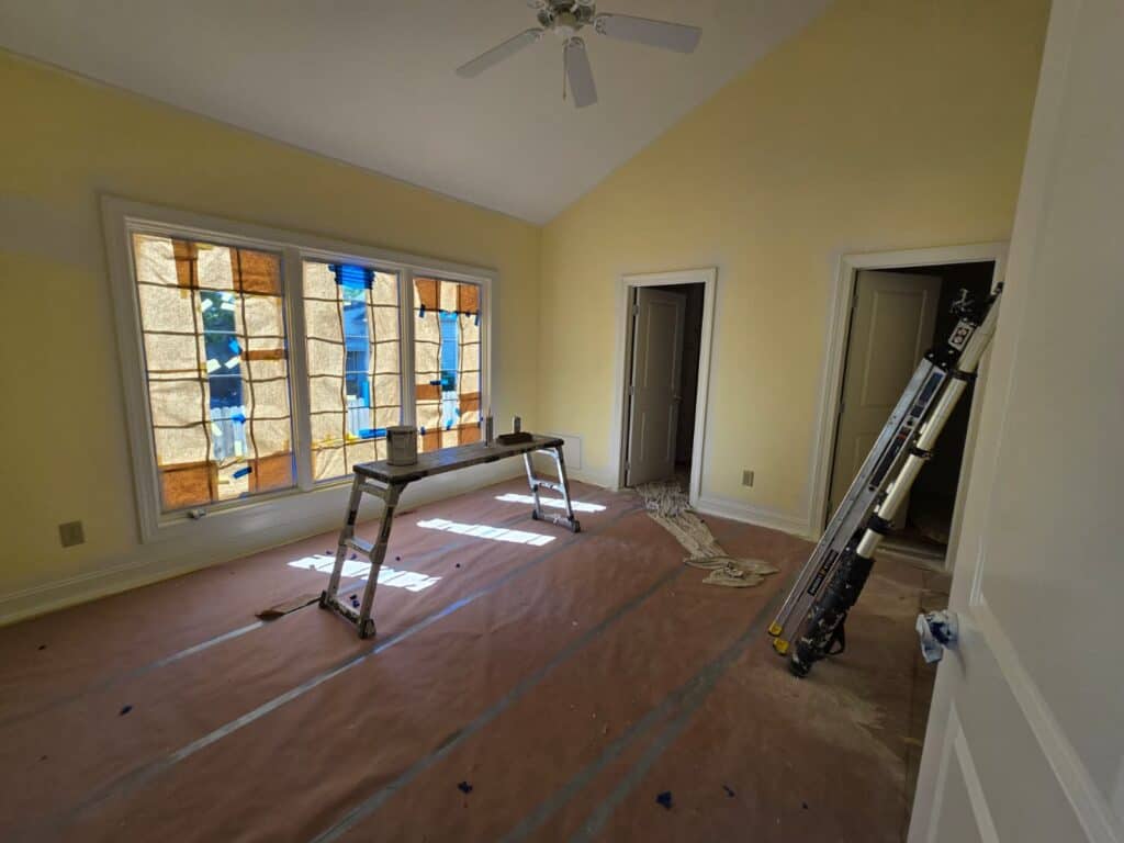 Interior painting renovation in progress, showing freshly painted yellow walls and window coverings.