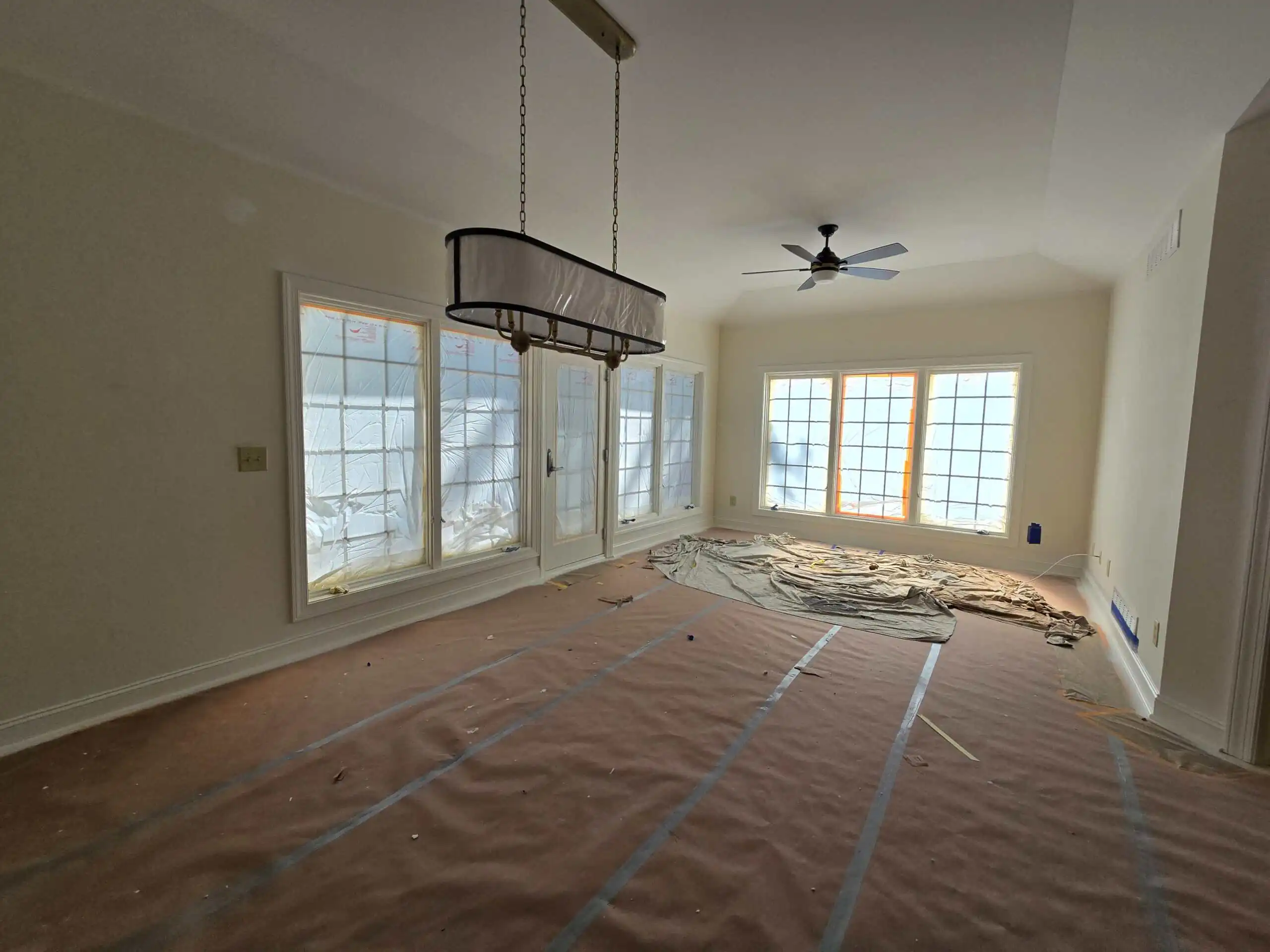 Dublin Ohio dining room prepared for interior painting — drop cloths cover floor, windows masked with paper, chandelier hanging